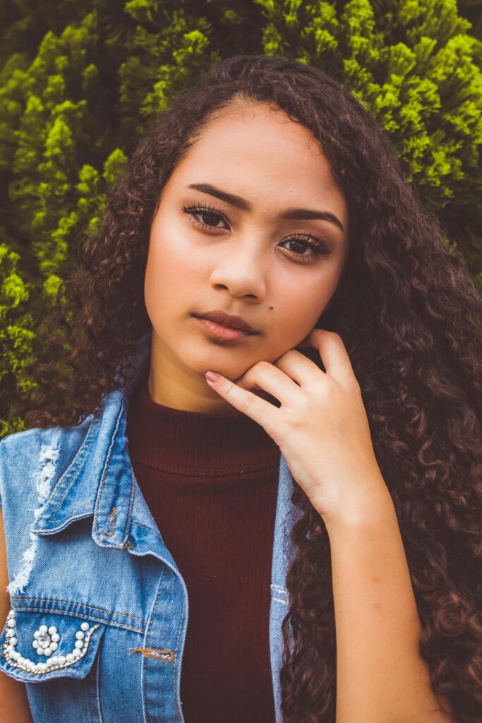 Close-up portrait of a teen girl with curly hair and thoughtful expression, outdoors.